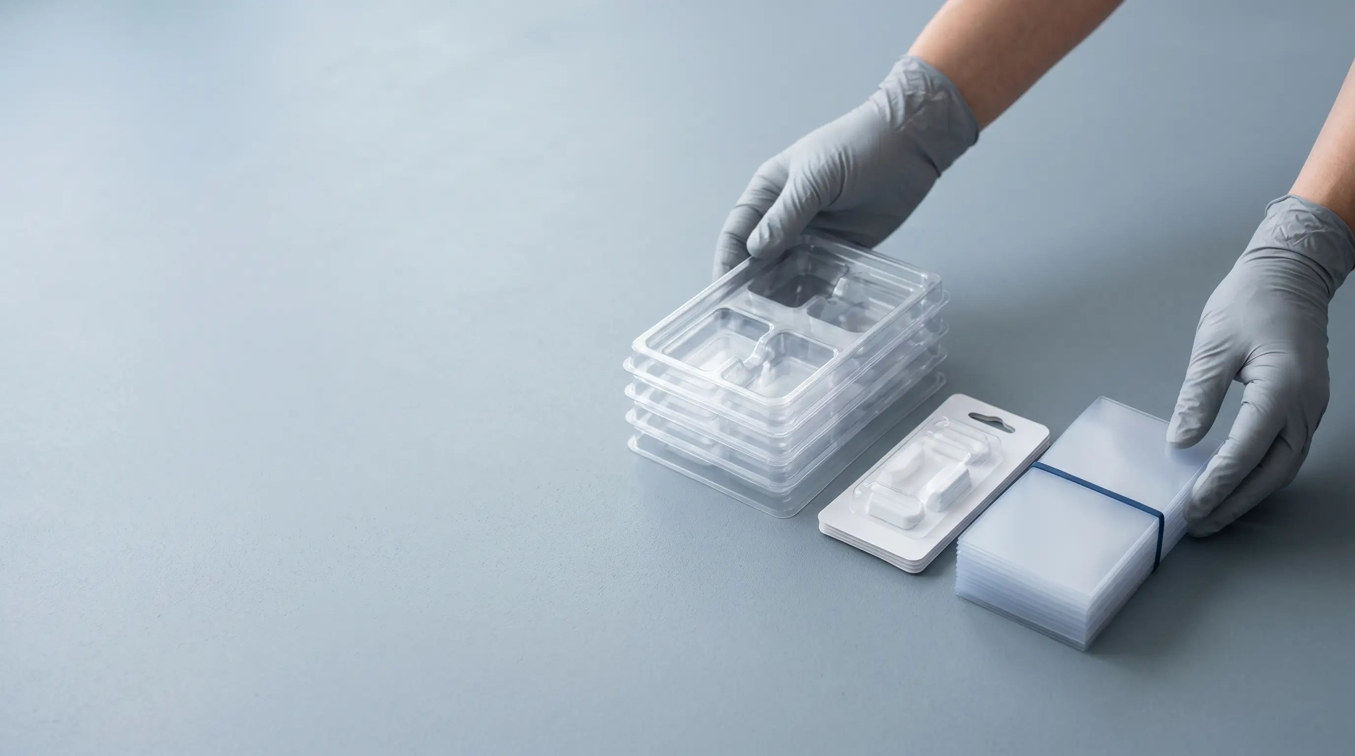 Gloved hands presenting thermoformed trays, a blister pack and PETG sheets